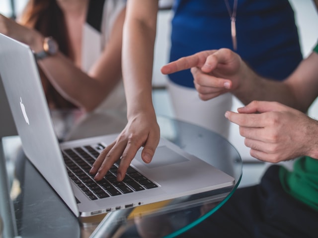 three people looking at something on a laptop as someone points to the screen