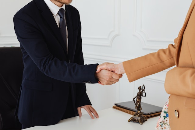 two people shaking hands across a desk that has a status of lady justice