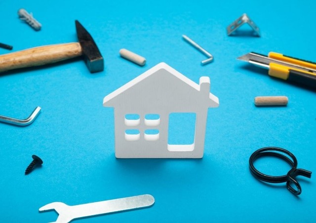 white-two-dimensional-house-standing-up-with-tools-around-it-with-a-teal-background