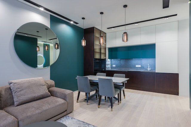 apartment with a blue accent wall, round mirror, light wood flooring and a brown couch