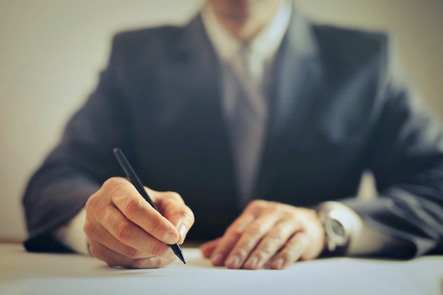 person in a dark suit writing something on a piece of paper