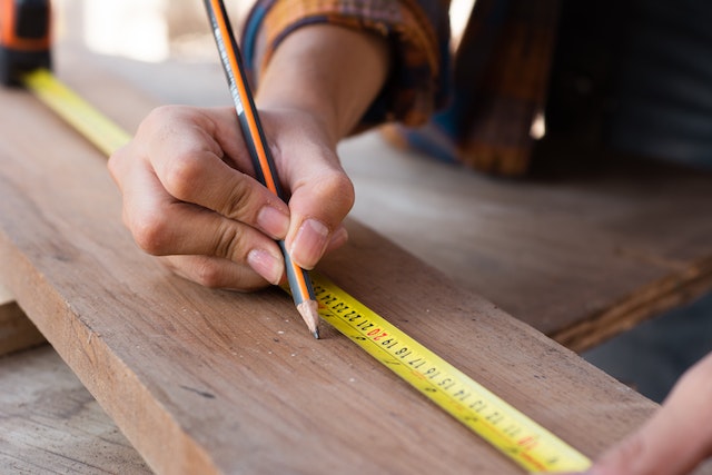 person using a pencil and measuring tape to make marks on a piece of wood