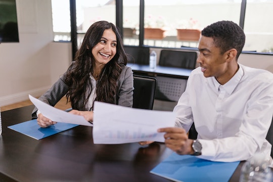 two people sitting side-by-side holding documents and smiling at each other