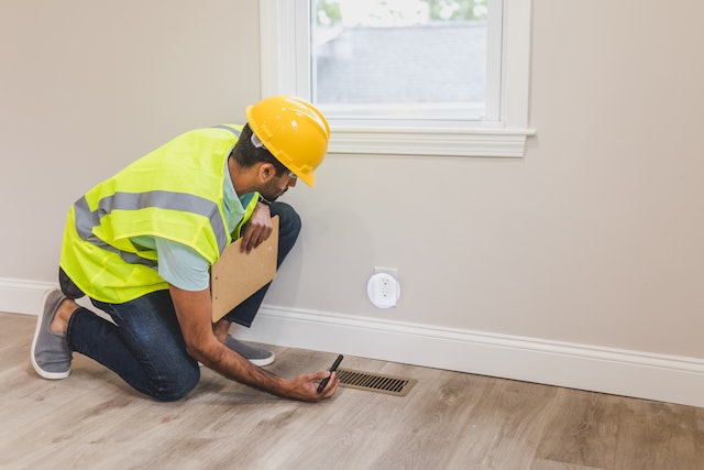 property inspector in a yellow vest and hardhat looking at a home's vents