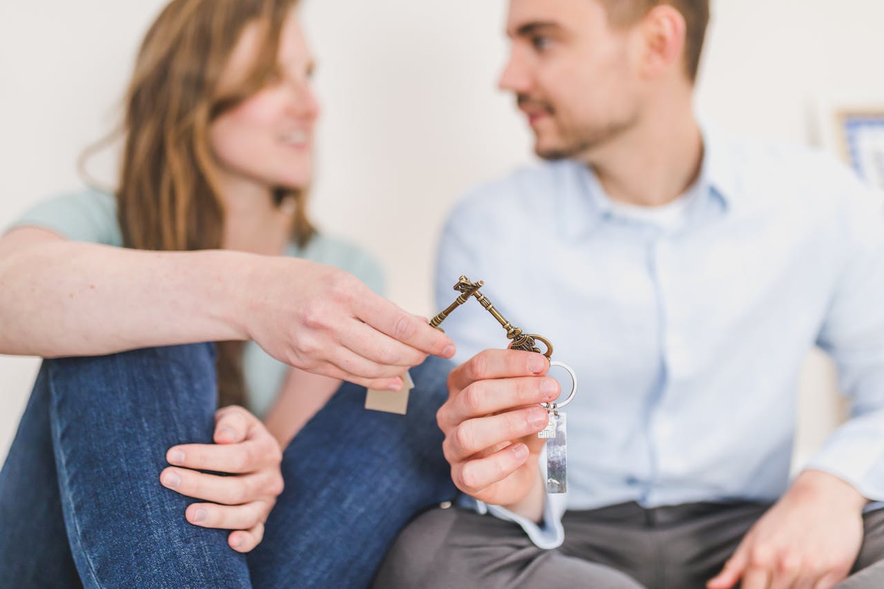 a-couple-sitting-together-and-smiling-while-holding-an-ornate-key-with-a-keychain-suggesting-they-ve-just-received-or-exchanged-keys-to-a-new-home