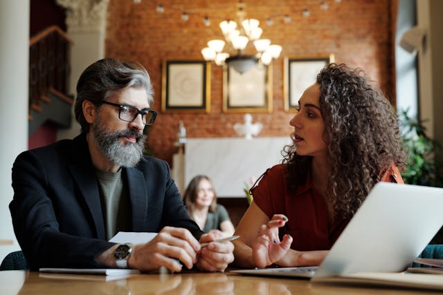 a-man-and-a-woman-sitting-at-a-table-discussing-something-with-a-laptop-in-front-of-them