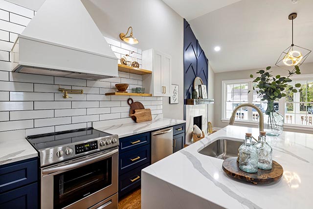 modern-kitchen-with-navy-blue-lower-cabinets-white-countertops-a-stainless-steel-oven-and-decorative-open-shelving-featuring-a-large-island-with-a-sink-and-glass-bottles