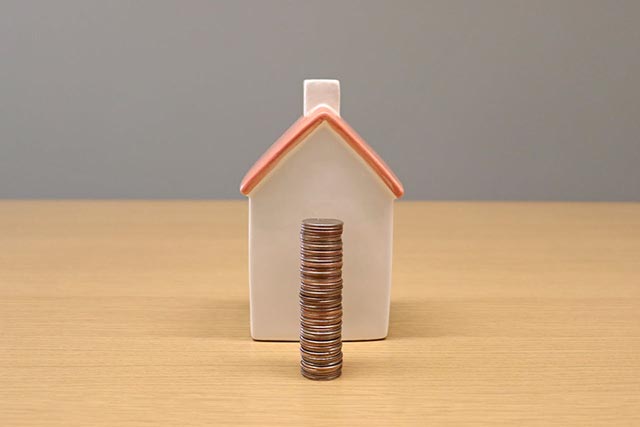 stack-of-coins-in-front-of-a-small-ceramic-house-on-a-wooden-surface