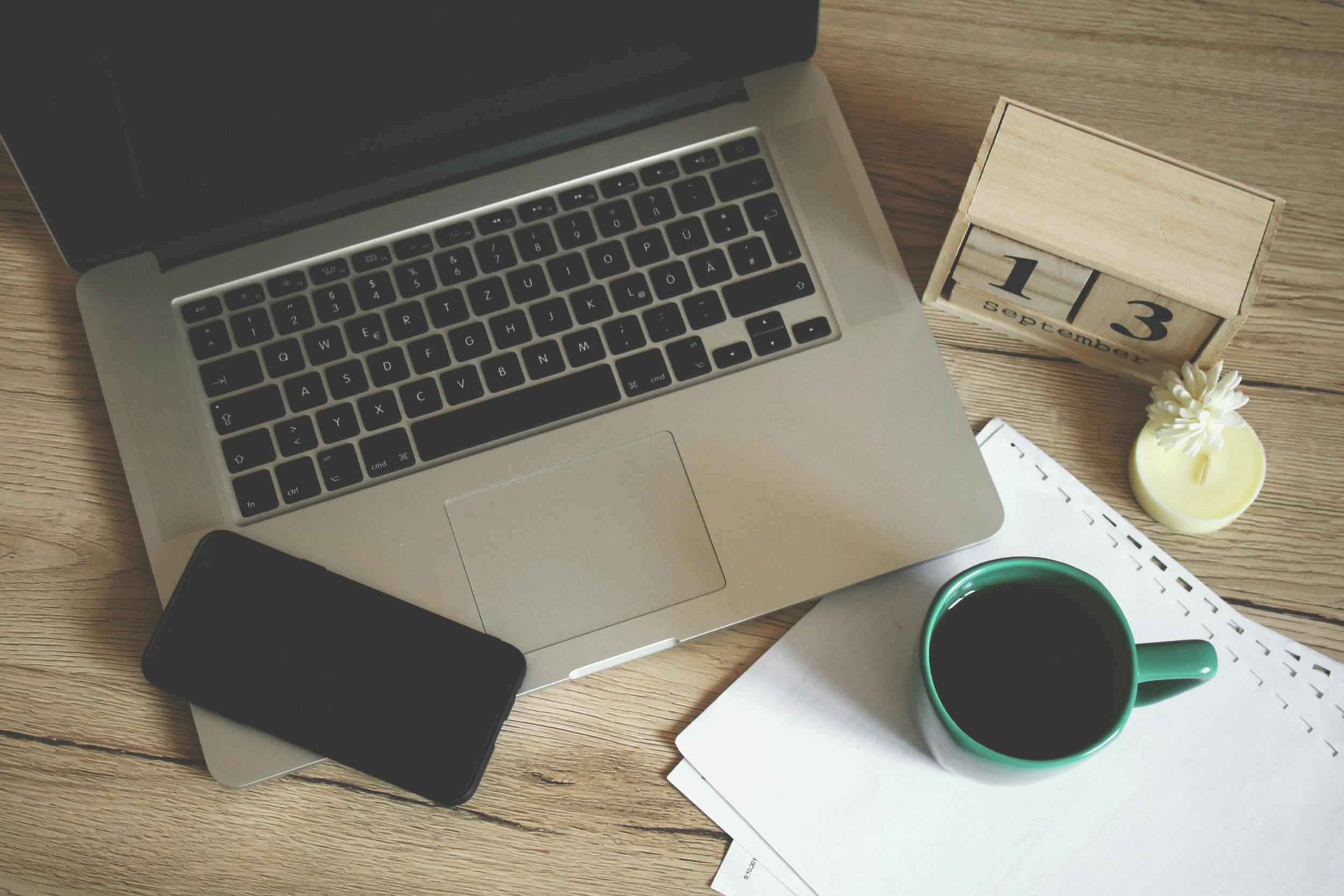 Overview of a laptop, cell phone, and cup of coffee on a desk.