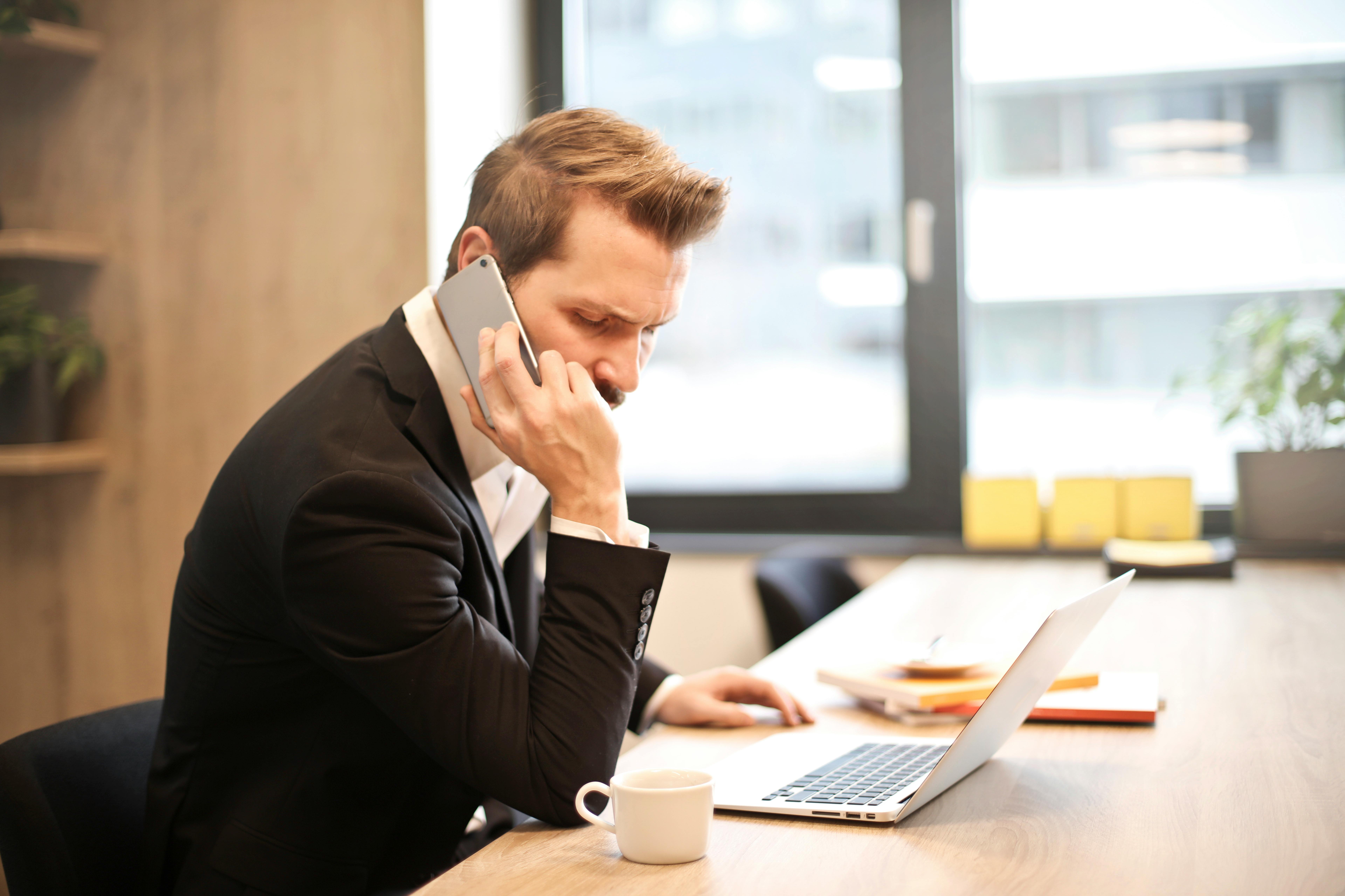 A man talking on his cell phone while sitting at a desk.