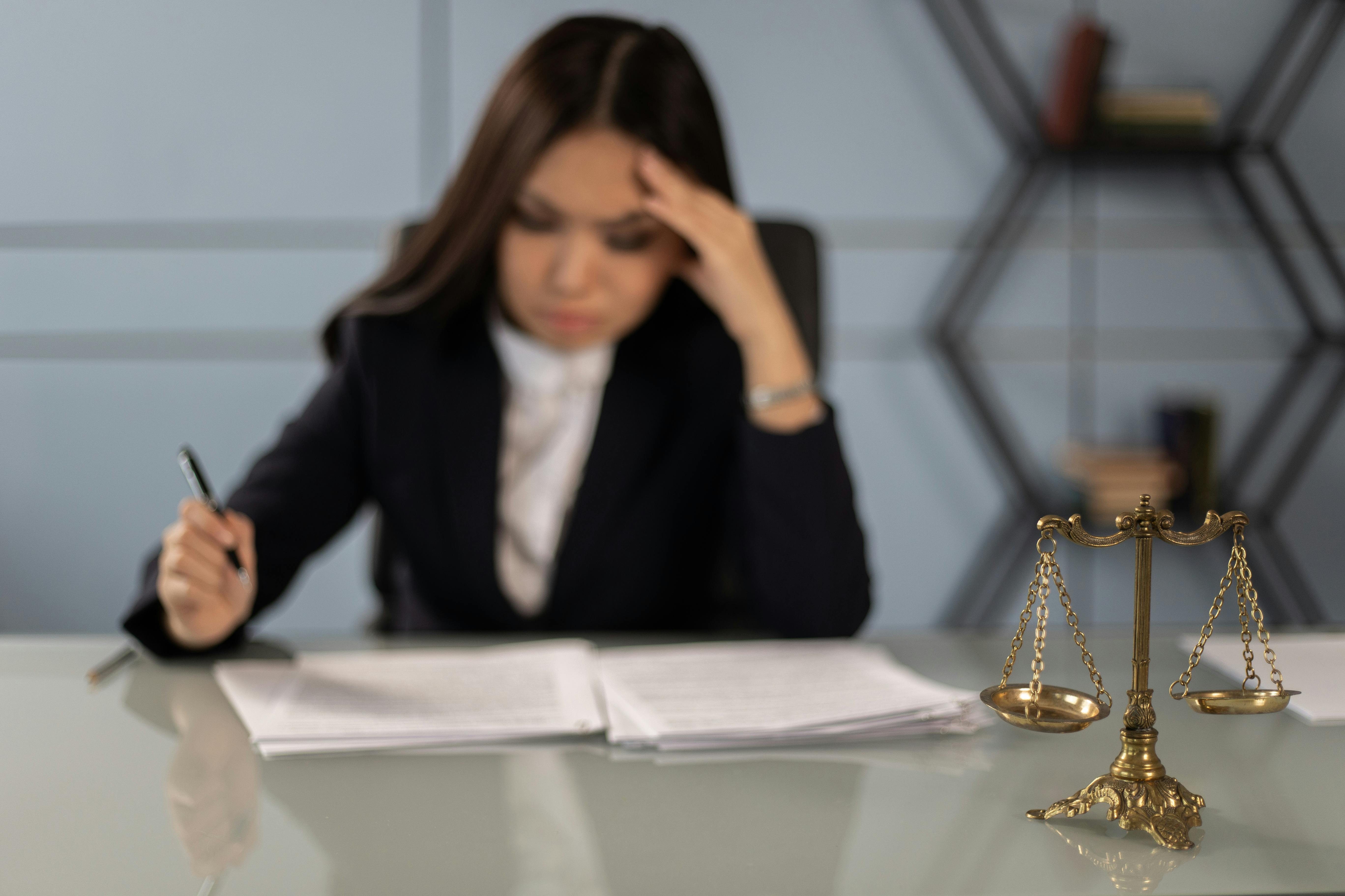 A scales of justice statuette on the desk of a professional woman reading paperwork.