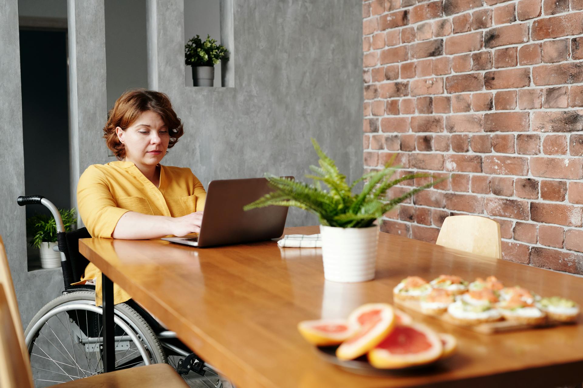 A person in a wheelchair sitting at their dining room table working on a laptop.