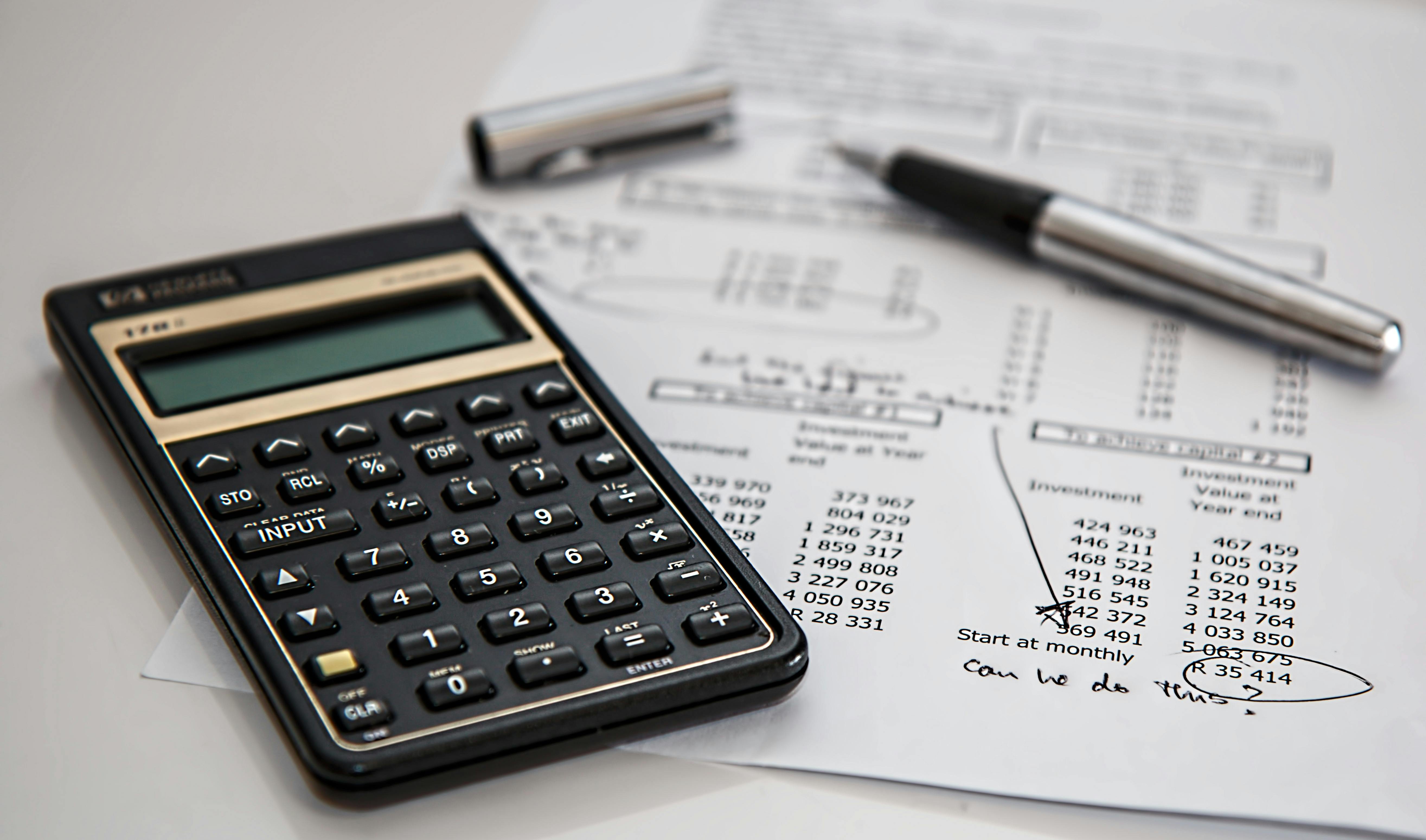 A calculator, pen, and financial documents on a desk.